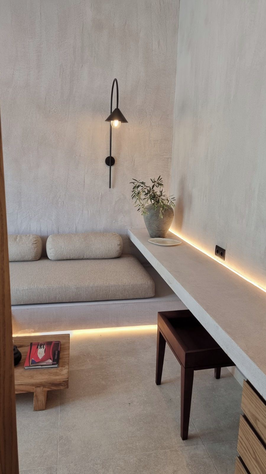 Ein modernes Wohnzimmer mit einer Couch, einem Beistelltisch, einem kleinen Holztisch mit einem Buch, einer Topfpflanze und einer Wandleuchte.