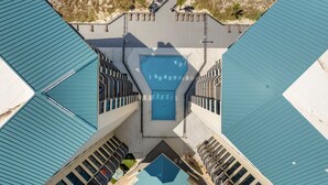 An aerial view of a hotel with a central swimming pool, surrounded by balconies and a beach area.