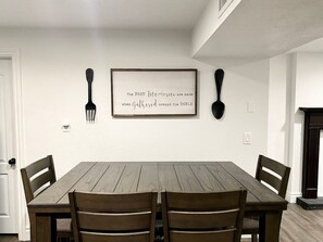 A dining room with a wooden table and four chairs, a framed quote on the wall, and a fireplace.
