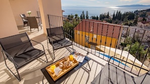 Un balcon avec une table préparée pour le petit-déjeuner, une chaise et une vue sur la mer et les bâtiments.