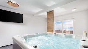 Une salle de bain moderne dotée d’un jacuzzi, d’un téléviseur à écran plat et d’une grande fenêtre offrant une vue sur la ville.