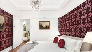 A bedroom with a large bed, a nightstand, a lamp, a painting, and a patterned wallpaper. - ART DECO BAYSIDE APARTMENT CLOSE TO THE CITY (Elizabeth Bay)