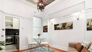 A modern living room with a dining area, wooden flooring, a chandelier, and artwork on the walls. - ART DECO BAYSIDE APARTMENT CLOSE TO THE CITY (Elizabeth Bay)