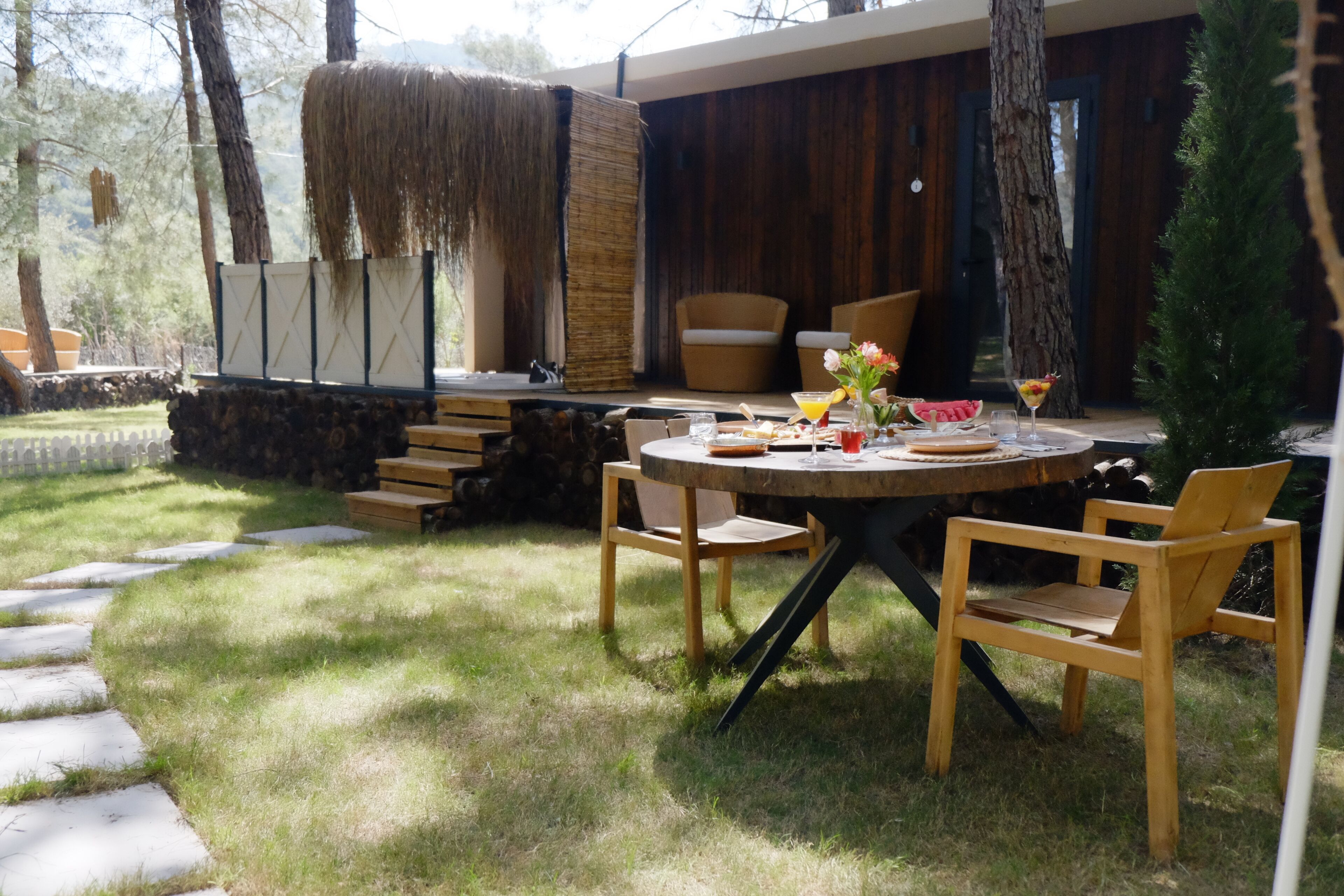 Un espacio de comedor al aire libre con una mesa redonda de madera, sillas y un muro de paja.