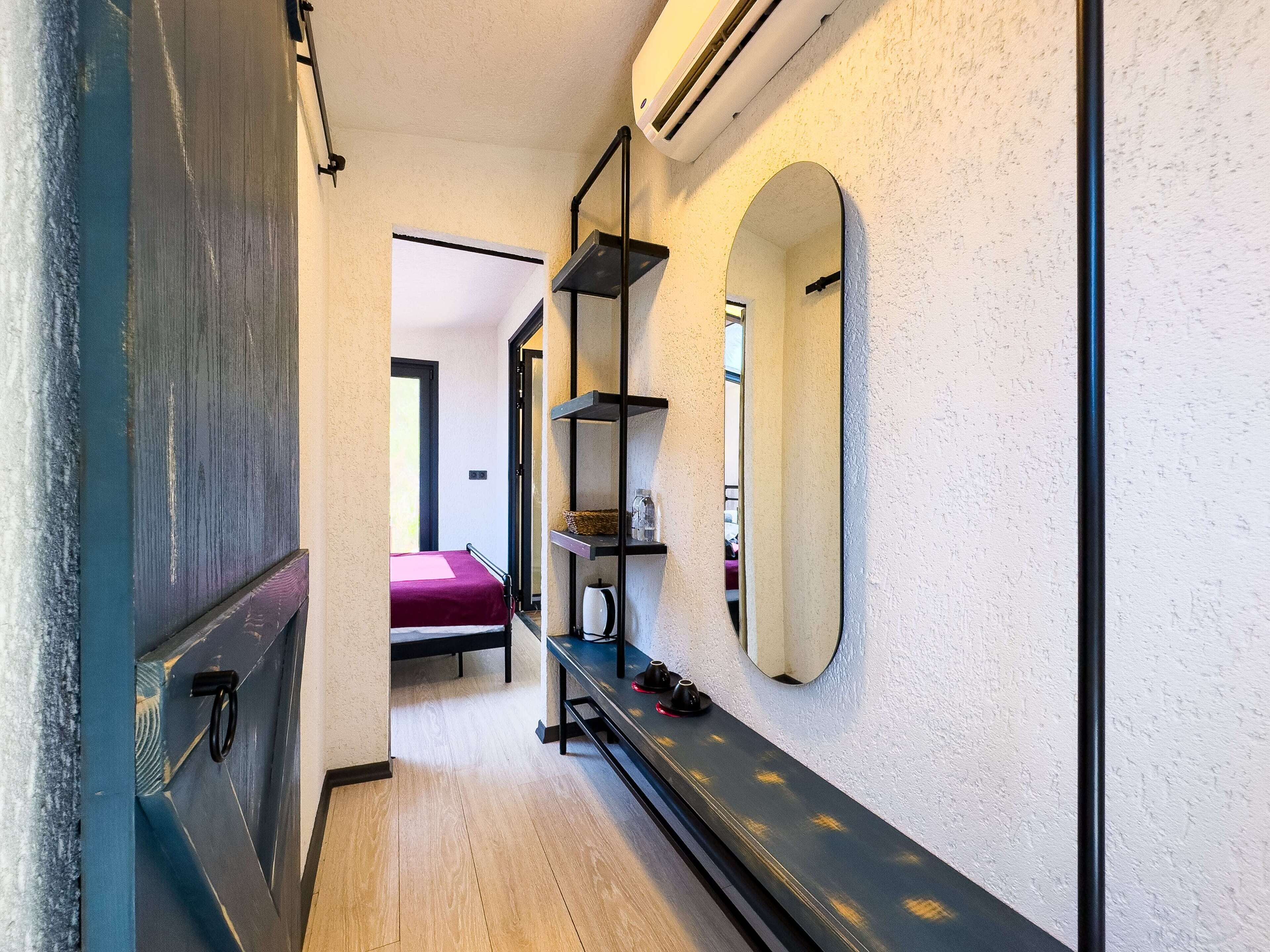 A narrow hallway with a bed, a mirror, shelves, and a door.