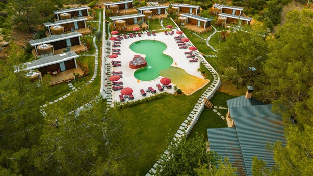 An aerial view of a resort with multiple bungalow-style buildings, a central swimming pool, and sun loungers. - Mossa Afkule (Fethiye)