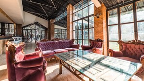 A spacious room with a large glass table and plush red sofas, featuring a high ceiling with exposed beams and large windows offering natural light. - Mossa Afkule (Fethiye)