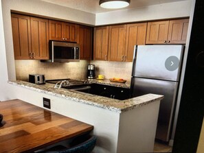 Kitchen area with a refrigerator, stove, microwave, and toaster, as well as a sink and granite countertop.