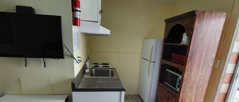A compact kitchen with a tiled floor, a built-in stove, a sink, and a refrigerator.