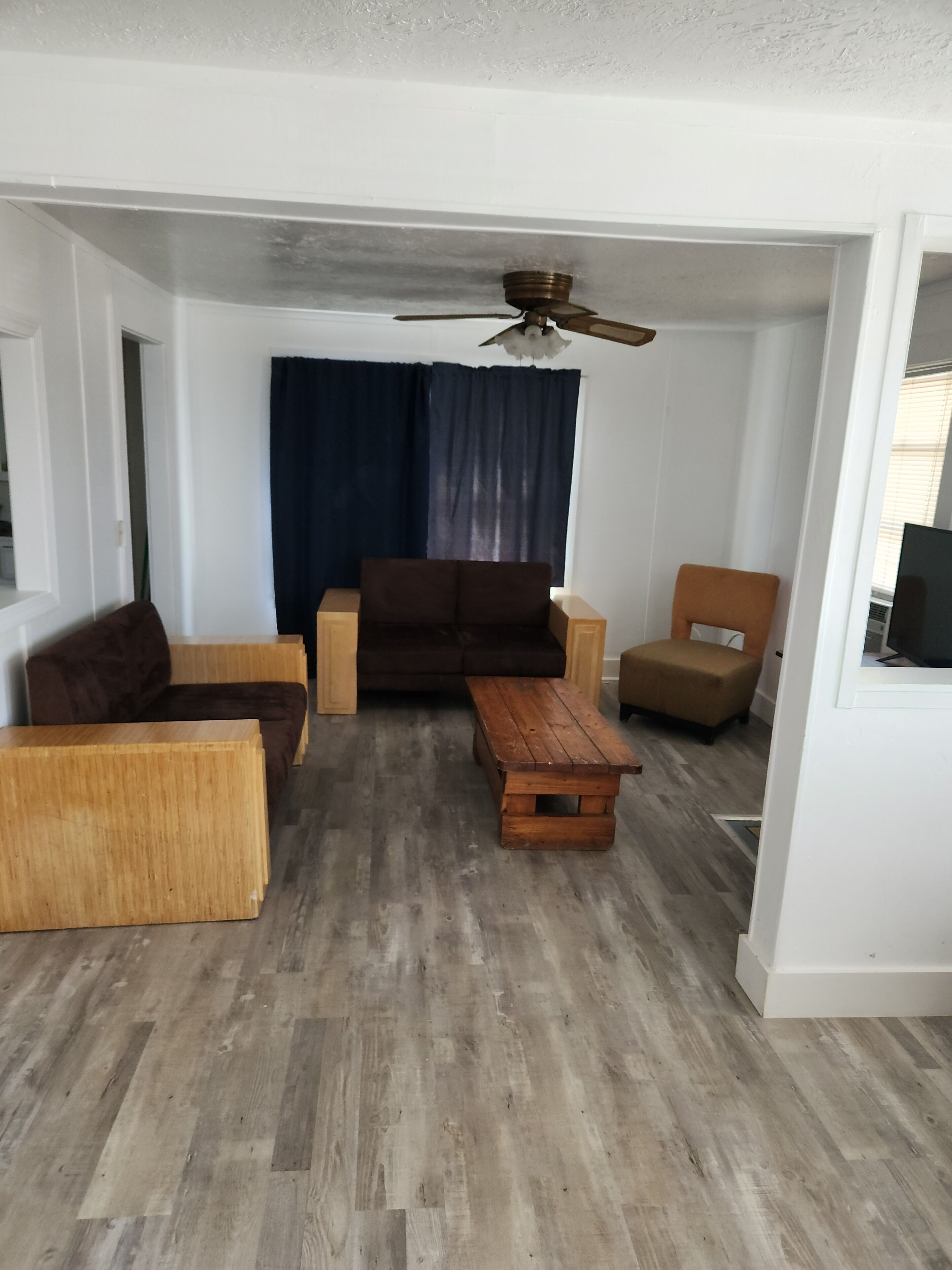 Un salon avec un canapé marron, une table basse en bois et un ventilateur de plafond.