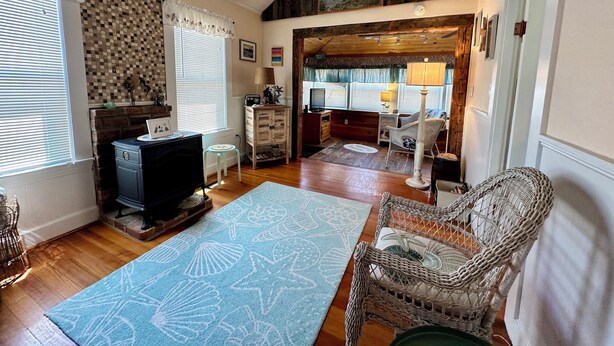 A cozy living room with a fireplace, a large rug, wicker furniture, and a painting of a lighthouse.