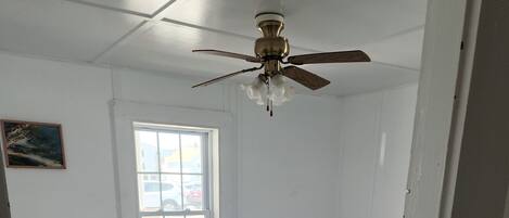 A room with two beds, a ceiling fan, a window, and a painting on the wall.