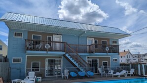 A two-story house with a pool, featuring a wooden deck and outdoor seating.