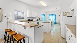 A modern kitchen with white cabinets, a wooden island with stools, a microwave, and a refrigerator. - New Listing! Highgate at Legacy Park Resort, 7mi to Disney & 10mi to Universal - FS370169 (Davenport)