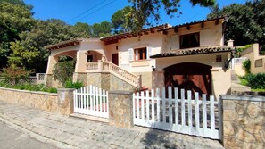 A two-story house with a stone facade, a white picket fence, and a tiled roof.
