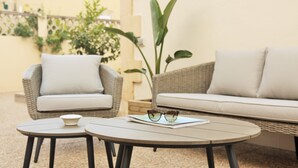 Un espace patio aménagé avec des meubles en osier, comprenant deux canapés et deux tables rondes, dont l’une est ornée d’une paire de lunettes.