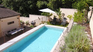 Une piscine rectangulaire avec un parasol blanc, entourée d’une clôture et agrémentée de plantes en pot.