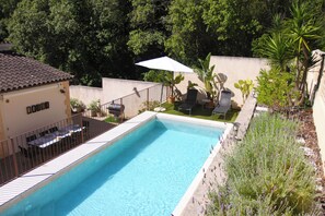 Ein rechteckiger Swimmingpool, umgeben von einem weiĂen Zaun, mit einer Terrasse, einem Tisch und StĂŒhlen sowie verschiedenen Topfpflanzen.