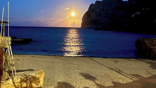 Une plage avec une structure en bois, une mer calme et un coucher de soleil.
