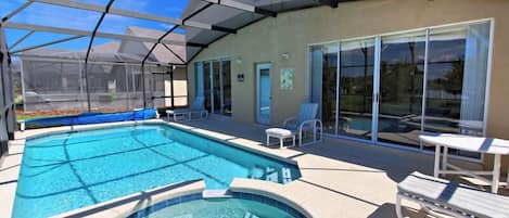 A covered outdoor swimming pool with lounge chairs and a hot tub.