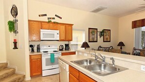 A kitchen with wooden cabinets, a white stove, a microwave, and a double sink.