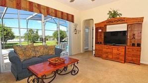 A living room with a sofa, coffee table, TV stand, and a glass door leading to a patio.