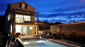 Uma casa de dois andares com piscina, varanda e muro de pedra.