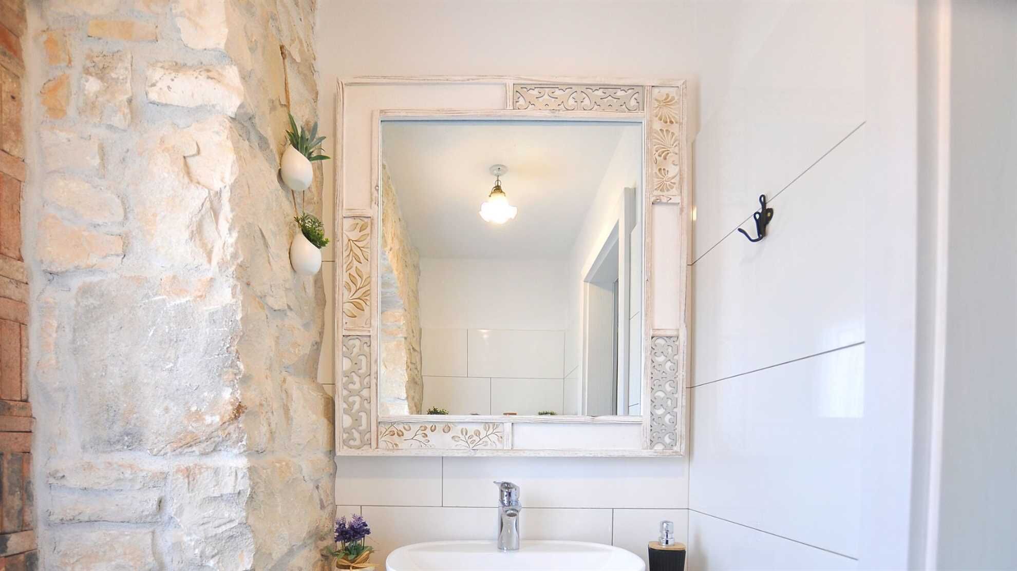 A bathroom with a stone wall, a white sink, and a mirror with decorative frame.