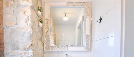 A bathroom with a stone wall, a white sink, and a mirror with decorative frame.