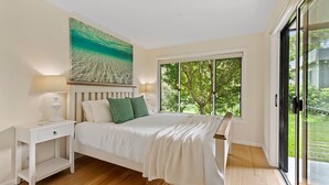 Ein Schlafzimmer mit einem Bett, Nachttischen, einem Gemälde und einem großen Fenster mit Blick auf Bäume.