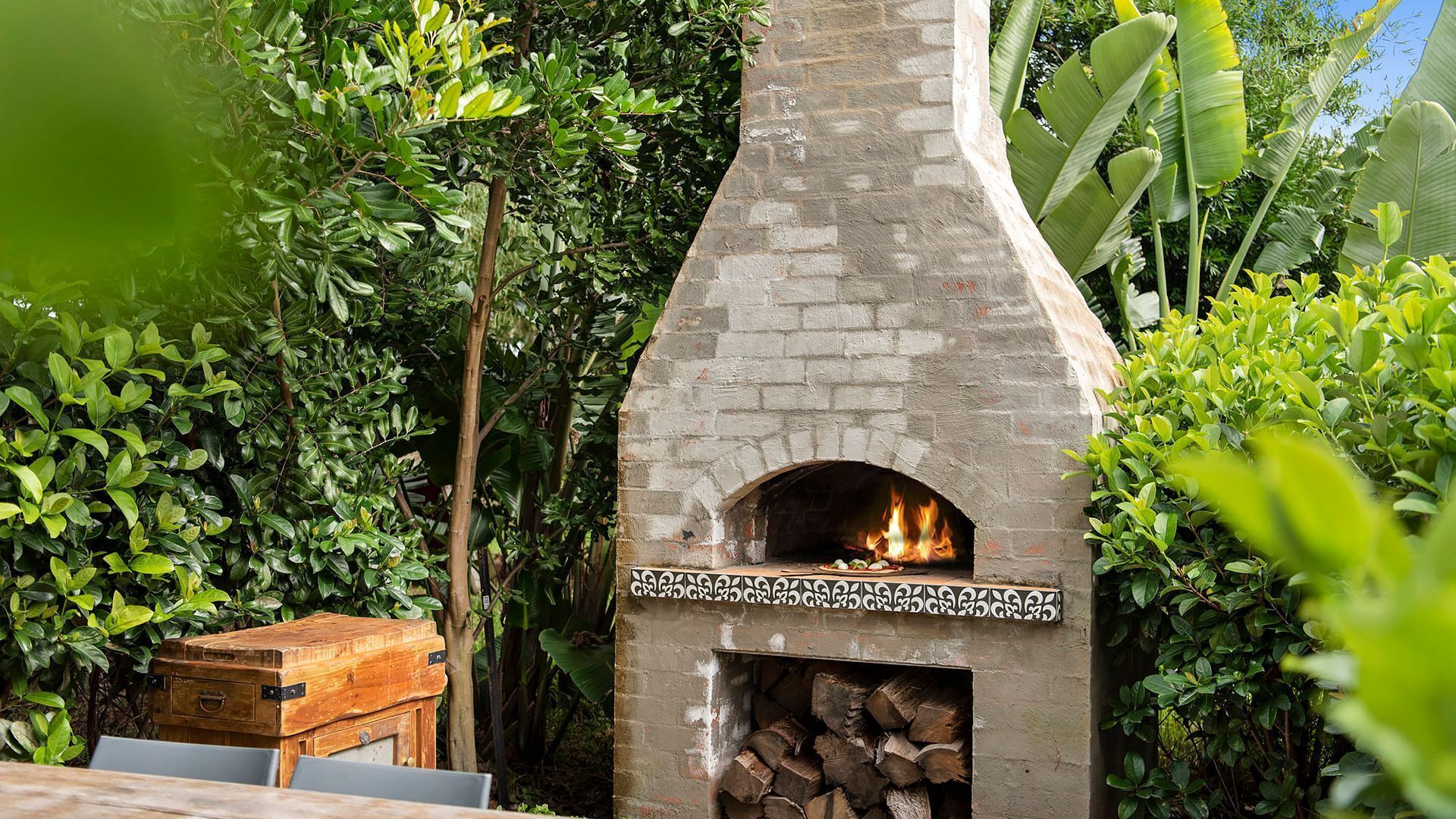 A brick-built outdoor pizza oven surrounded by lush greenery.