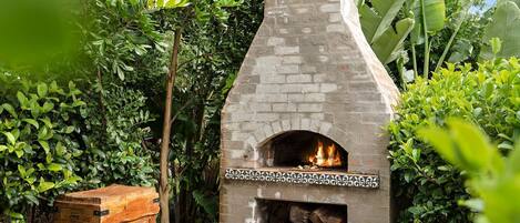 A brick-built outdoor pizza oven surrounded by lush greenery.