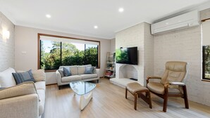 Una sala de estar moderna con un sofá, un sillón, una mesa de centro de vidrio y un televisor de pantalla plana montado en una pared de ladrillo.