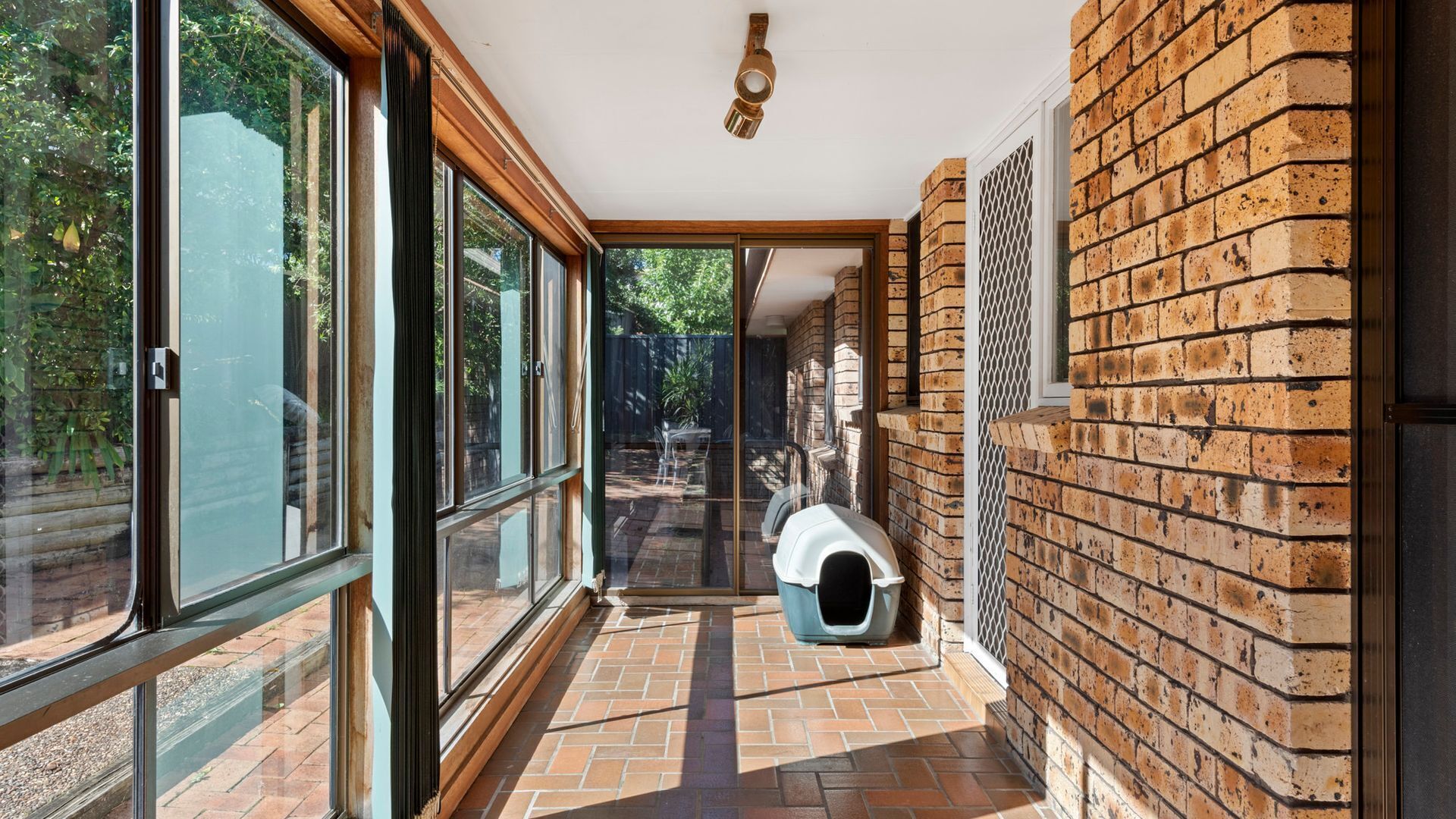 A narrow hallway with large windows, a brick wall, and a pet area with a cat house.