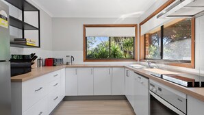 Una cocina moderna con armarios blancos, encimera de madera, horno empotrado y ventana con vistas a la vegetación.