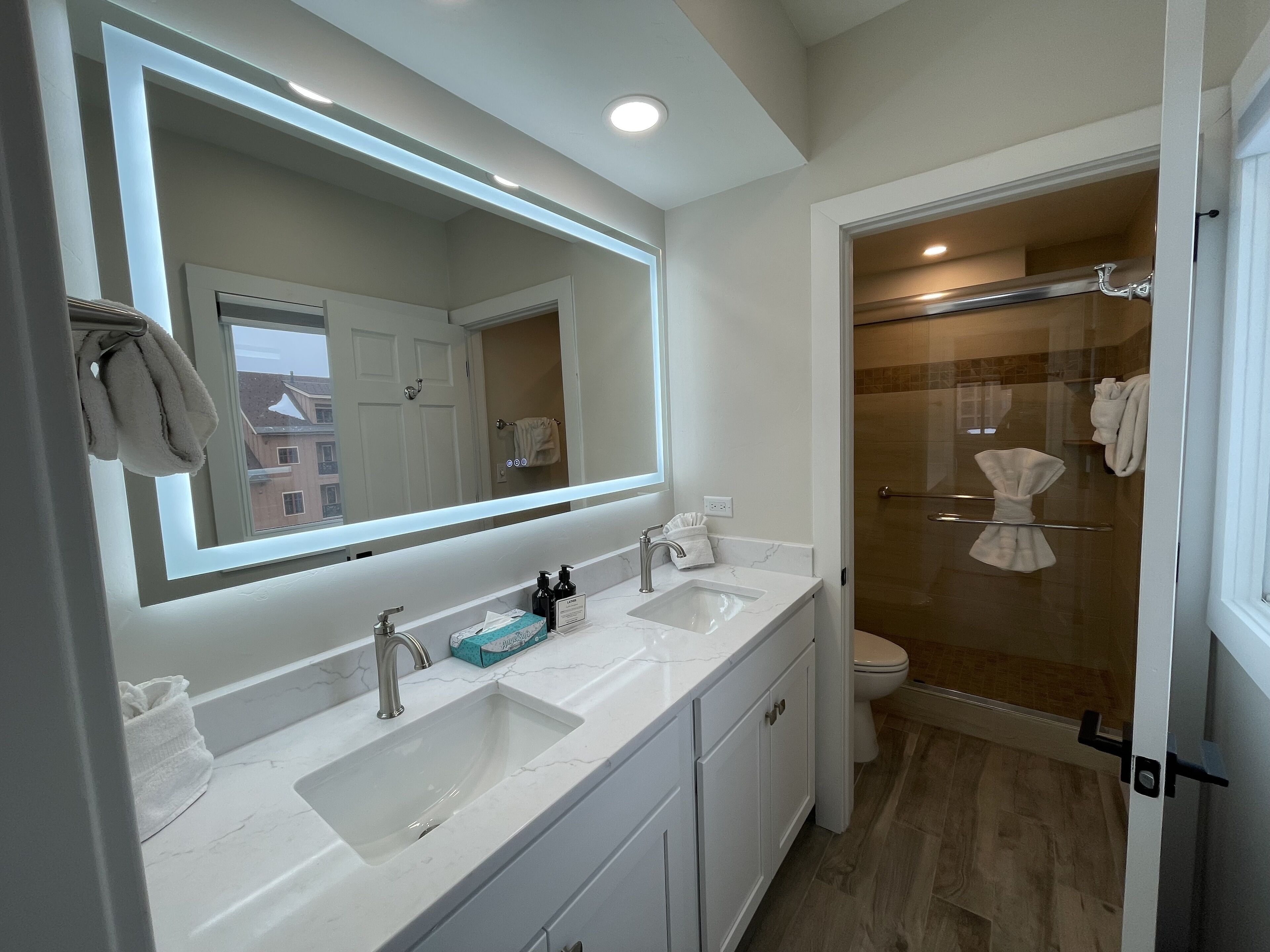 Un bagno moderno con un ampio specchio, due lavabi e cabina doccia in vetro.
