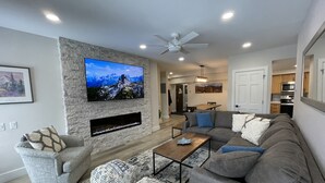 A modern living room with a flat-screen TV, a fireplace, a sofa, and a dining area in the background. - Bright Haus Lakeview at the Village at Breck ,Stunning Views, Ski In/Out In Town (Breckenridge)