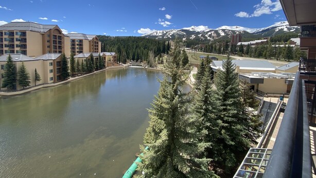 A view of a resort with a lake, buildings, and snow-capped mountains in the background. - Bright Haus Lakeview at the Village at Breck ,Stunning Views, Ski In/Out In Town (Breckenridge)