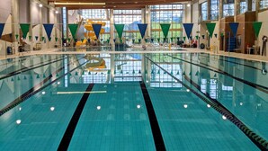 En stor indendørs swimmingpool med tydelige baner, trælofter og store vinduer med udsigt til det fri.