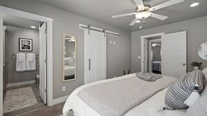 A bedroom with a bed, a ceiling fan, a large mirror, and a door leading to a bathroom.