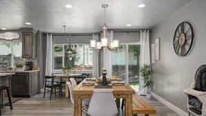 A dining area with a wooden table, chairs, and a chandelier. There is a kitchen area with a sign that reads "BISTRO".
