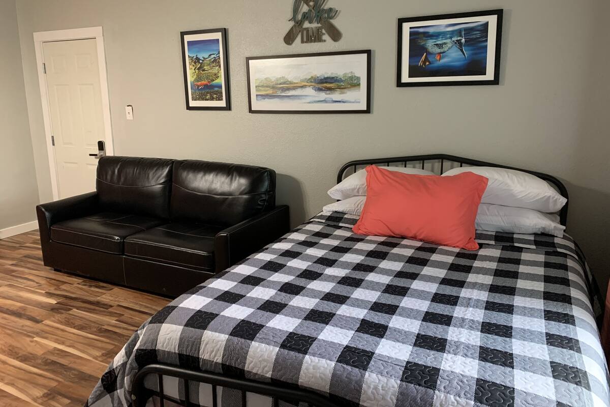 A bedroom with a black leather couch, a checkered bedspread, and three framed pictures on the wall.