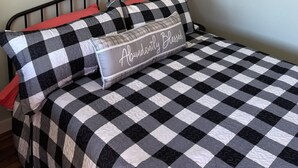 Un letto rifatto con cura, coperto da una trapunta a quadri e con un cuscino che riporta la scritta “Abundantly Blessed”, affiancato da due vasi da parete con piante verdi.