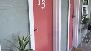 Una fila di porte con i numeri 13 e 4, piante in vaso e un tappetino d'ingresso.