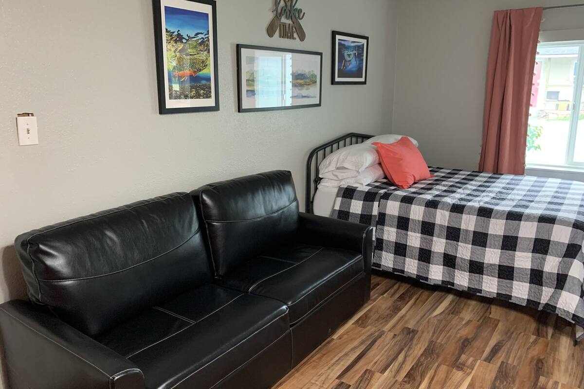 A room with a black leather sofa, a bed with a checkered bedspread, and three framed pictures on the wall.