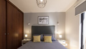 A bedroom with a large bed, two bedside lamps, a framed picture on the wall, and a window on the right.