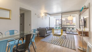 A modern living room with a glass dining table, grey sofa, and yellow chairs.