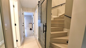 Un couloir avec une porte en bois, un escalier aux marches beiges et un plancher recouvert de moquette.