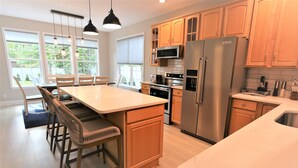 Une cuisine moderne dotée de meubles en bois, d’appareils électroménagers en acier inoxydable et d’un grand îlot central avec des sièges.