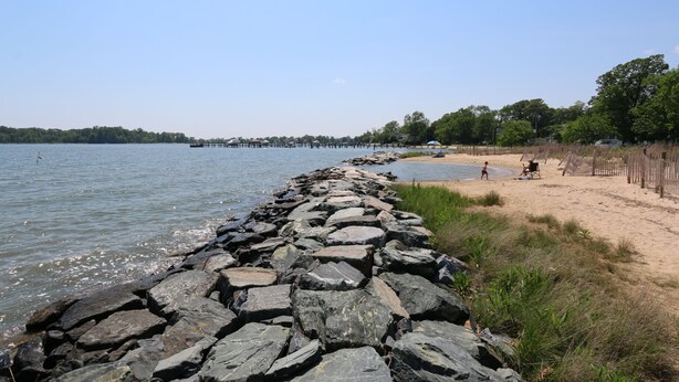 Une plage avec une digue rocheuse, un rivage sablonneux et une jetée visible au loin.